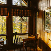 Sunlight streams through large windows, illuminating the interior table of a wooden cabin