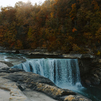 Long exposure of a waterfall cascading down, with smooth rocks in the foreground and yellow and orange trees behind.