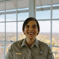 A female park ranger wearing a beanie smiles in a fire lookout tower.