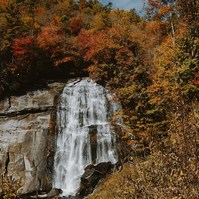 A huge waterfall flows down a rock face surrounded by Autumn trees