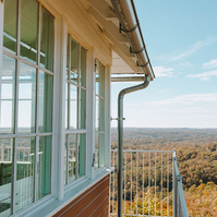 Exterior of the red fire tower, metal balcony and railings with Autumn coloured trees in the background.
