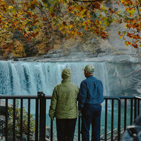 An elderly couple stand looking over a view point with a waterfall in the background.