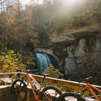 Two orange gravel bikes sit in front of a waterfall