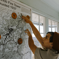 Woman points to pins on an old paper map on the wall 