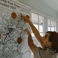 Woman points to pins on an old paper map on the wall 