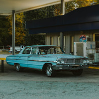 A rusty Ford Galaxy sits in a gas station with a small boy inside