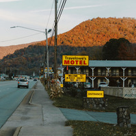 A yelow and red motel sign is lit up, while the morning sun hits the hills behind