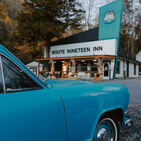 A vintage blue Kaiser sits in front of a retro style motel called Route 19 inn