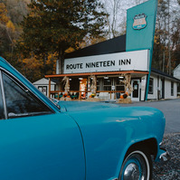 A vintage blue Kaiser sits in front of a retro style motel called Route 19 inn