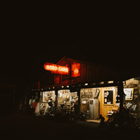 A neon 'used car' sign lights up the front of a junk yard office