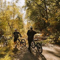 three people walk their bikes off a path around a fallen tree