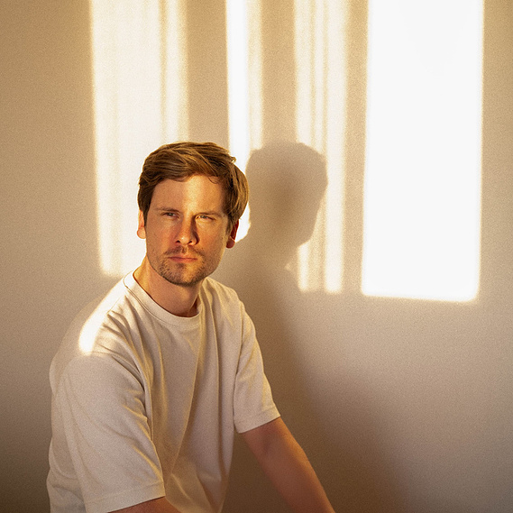 Portrait minimaliste et professionnel du photographe dans une lumière dorée, reflétant créativité et authenticité, placé sur la page ‘À propos’ d’un studio créatif dédié à l’immersion dans des reportages variés.