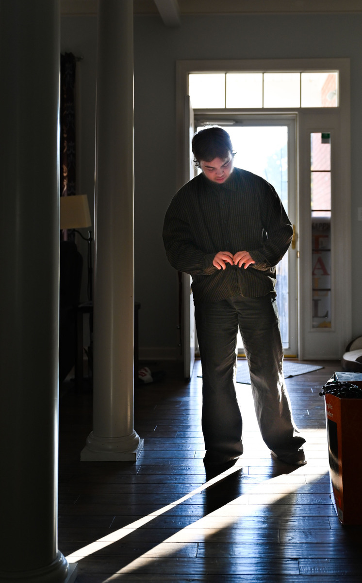Jay, backlit, buttons his shirt in the entryway of his home.