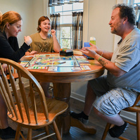 Jay, center, plays SpongeBob SquarePants Monopoly with his mom, Dena Castilow, left, and dad, Harry Castilow, right, at the Castilows’ kitchen table.