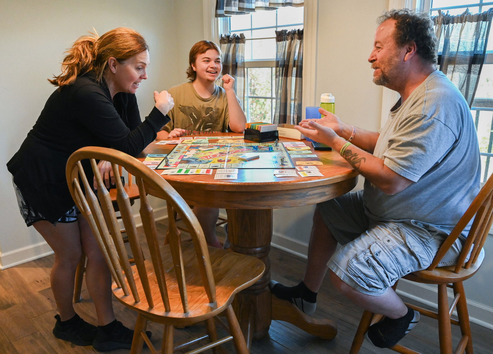 Jay, center, plays SpongeBob SquarePants Monopoly with his mom, Dena Castilow, left, and dad, Harry Castilow, right, at the Castilows’ kitchen table.