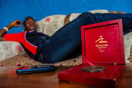 A blind athlete and two times paralympian sitting in his living room with his Beijing Olympic participation medal on the table.  Paralympic Sports Blind Athlete