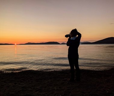 A woman photographing while standing on a beach at sunset. Copyright Tony Rix.