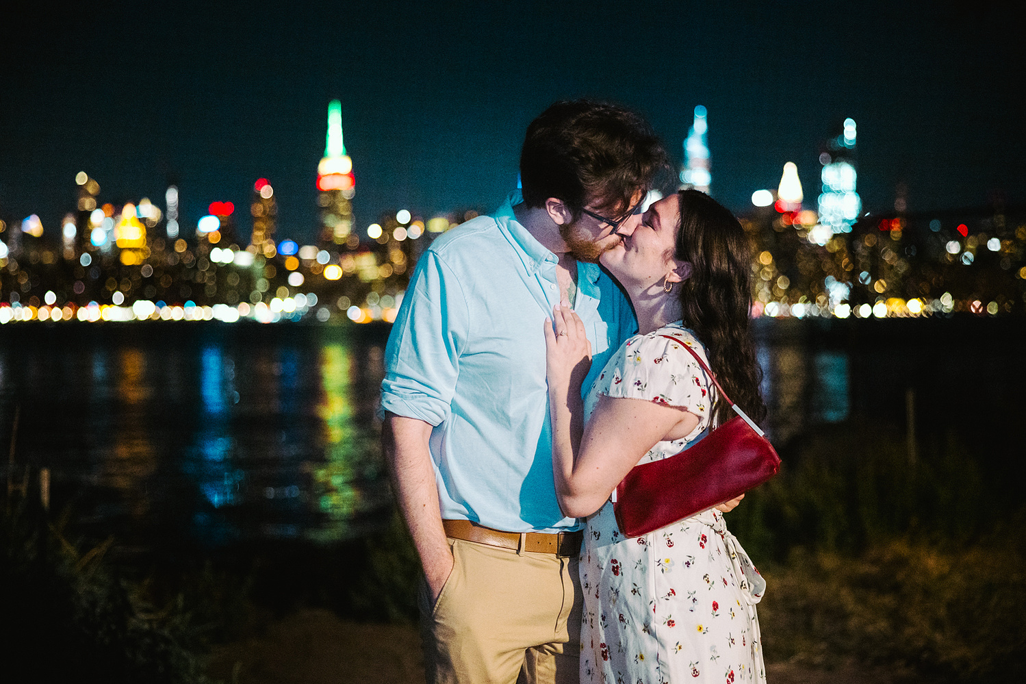 nighttime engagement session with the New York City skyline in the background, couple kissing for an engagement session by mc3 photo