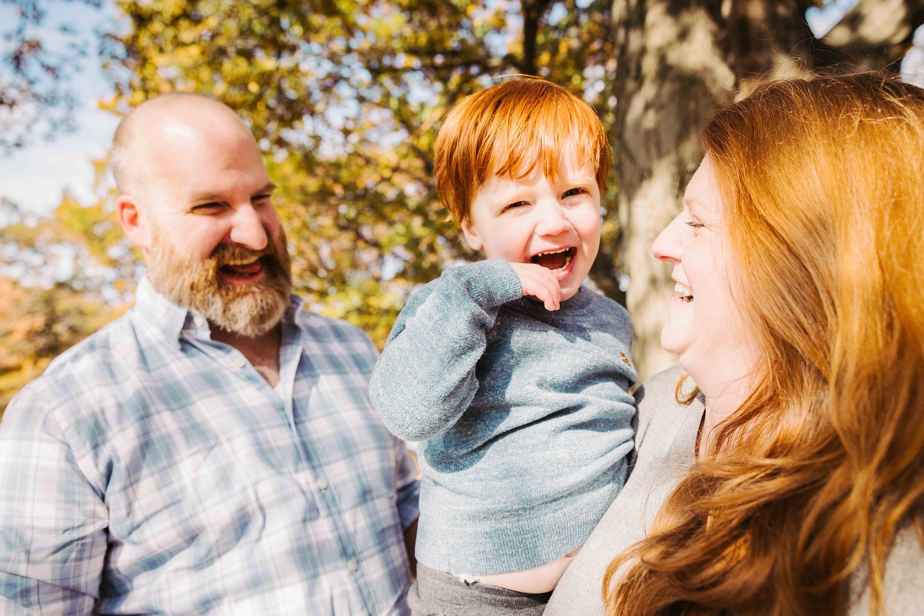 family of three laughing naturally and smiling in the fall, in Astoria park, queens. mc3 photo family portrait sessions 
