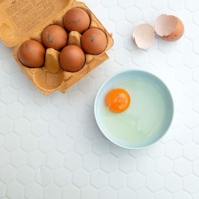 brown eggs in egg carton, one broken with egg in a bowl, orange yolk
