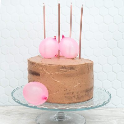 chocolate cake on cake stand with 4 candles and pink tiny ballons