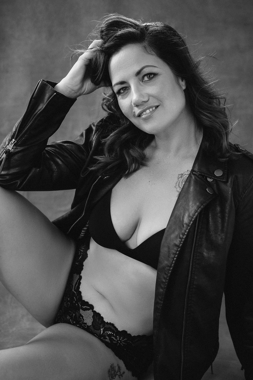 A glamourous young brunette woman poses in her lingerie with a leather jacket over the top