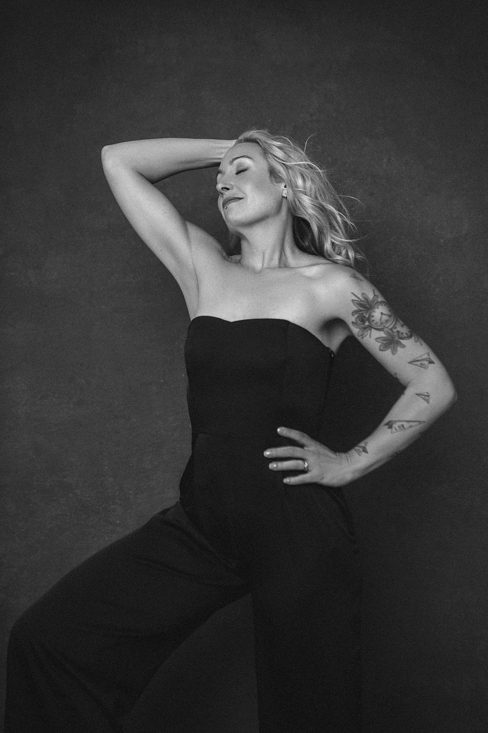 A quirky woman with long blonde hair poses powerfully, tattoos visible 