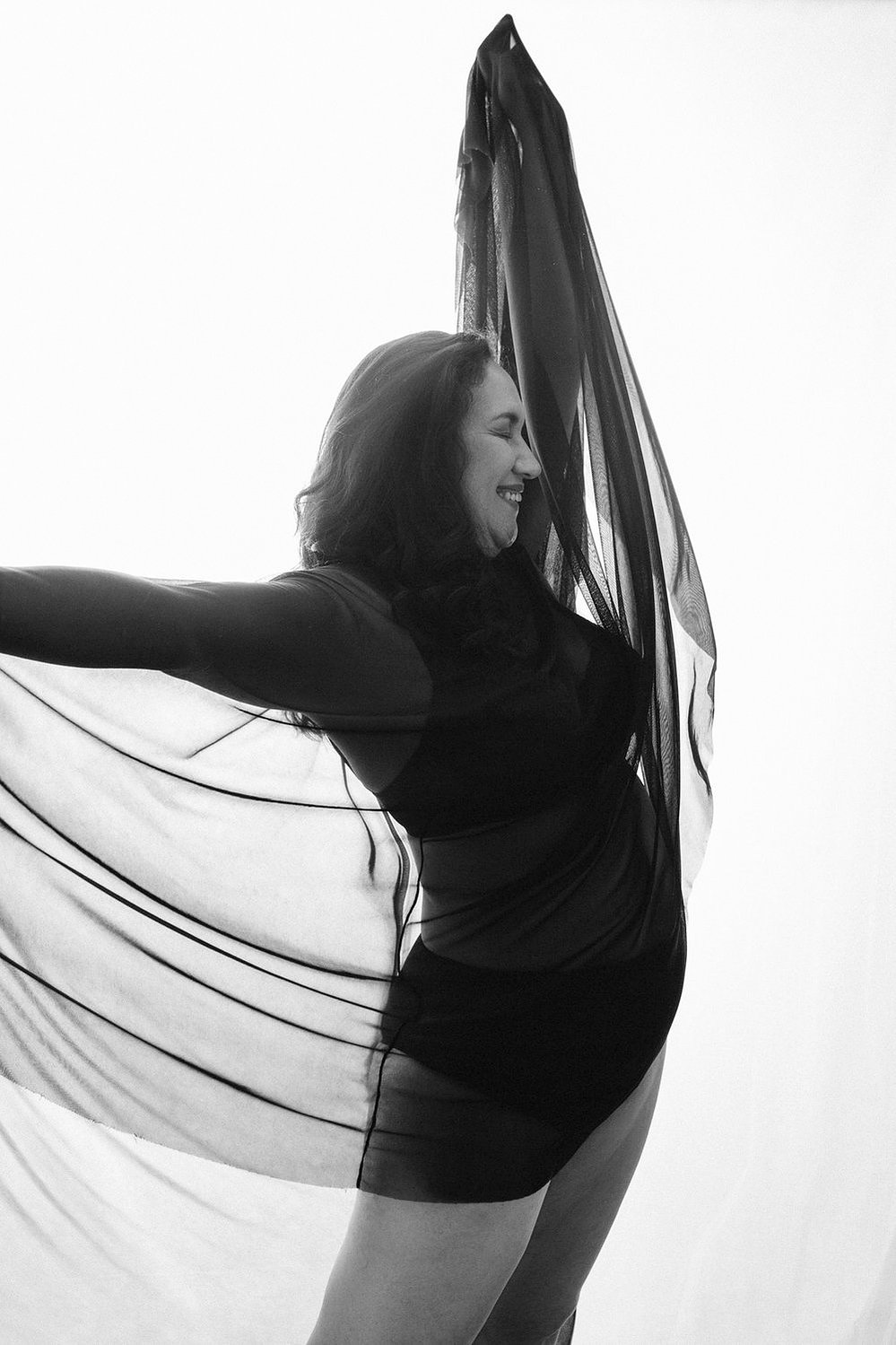 A stunning brunette woman wears a lacey bodysuit and sheer skirt, she dances and smiles
