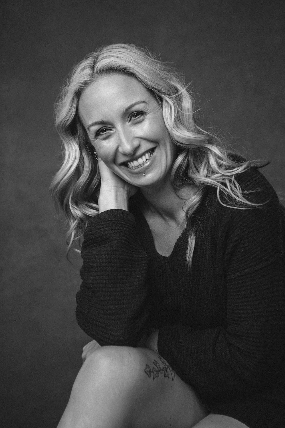 A quirky woman with long blonde hair smiles at the camera