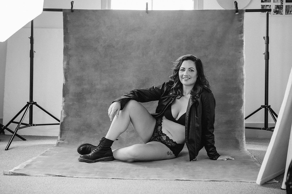 A glamourous young brunette woman poses in a leather jacket and funky boots