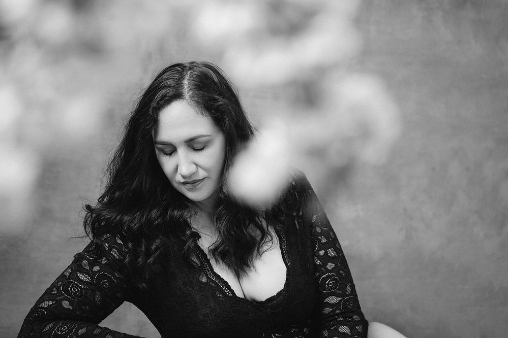 A stunning brunette woman wears a lacey bodysuit and is framed by spring blooms