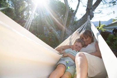 A woman and her grandson cuddle in a white hammock on a sunny summer evening