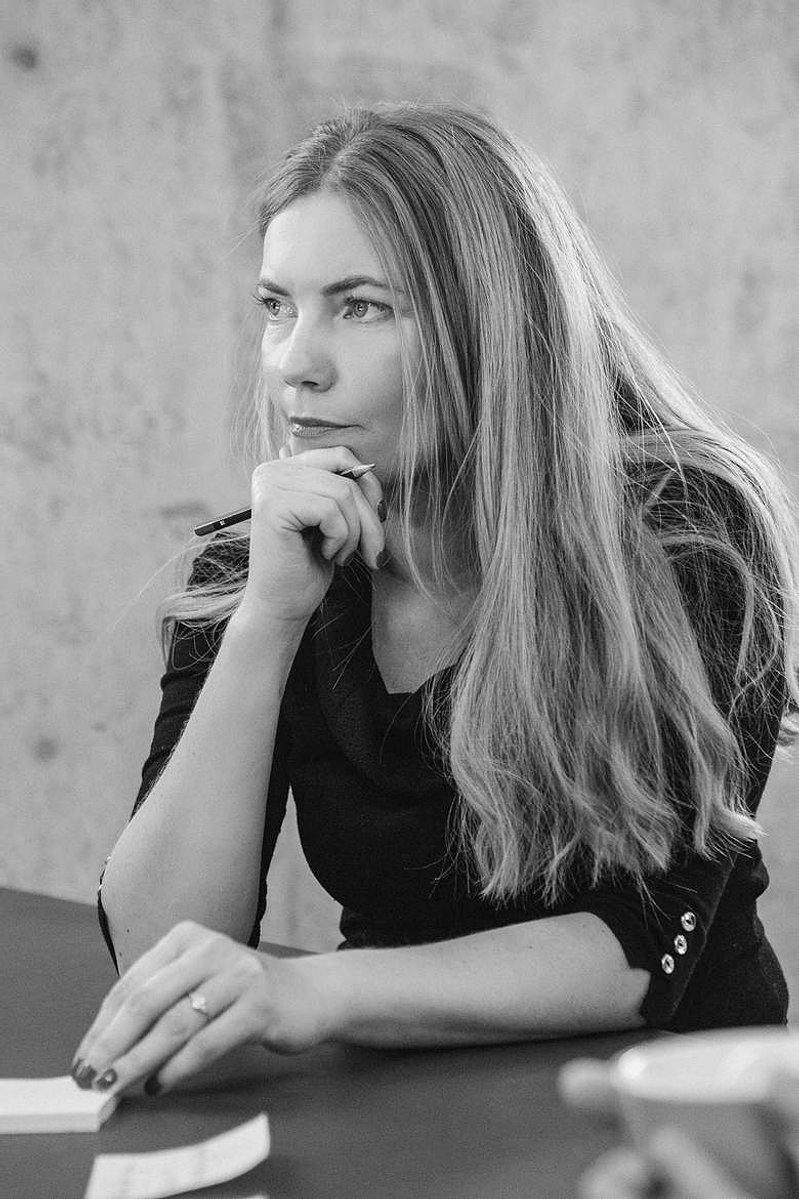 A blonde woman sits at a meeting table, she is listening intently to what others are saying
