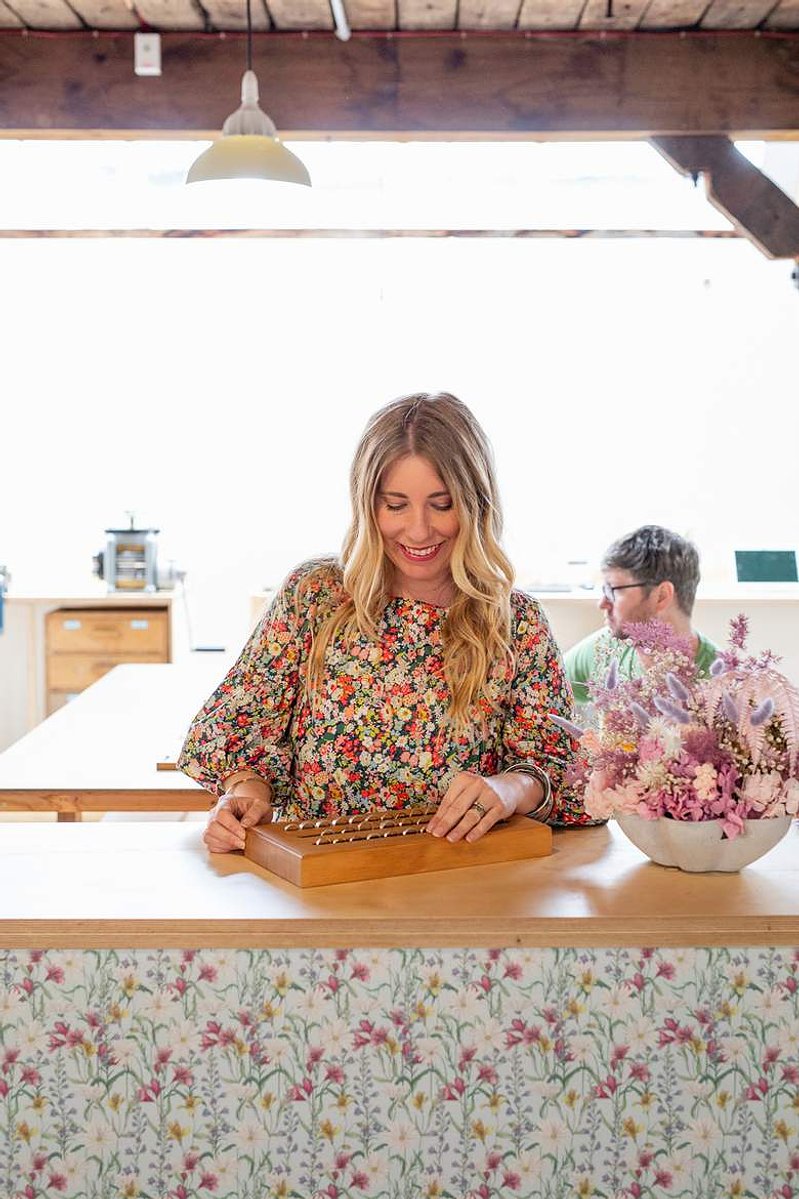 A blonde woman smiles contentedly as she looks down at a tray of handmade rings