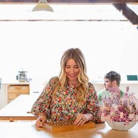 A blonde woman smiles contentedly as she looks down at a tray of handmade rings
