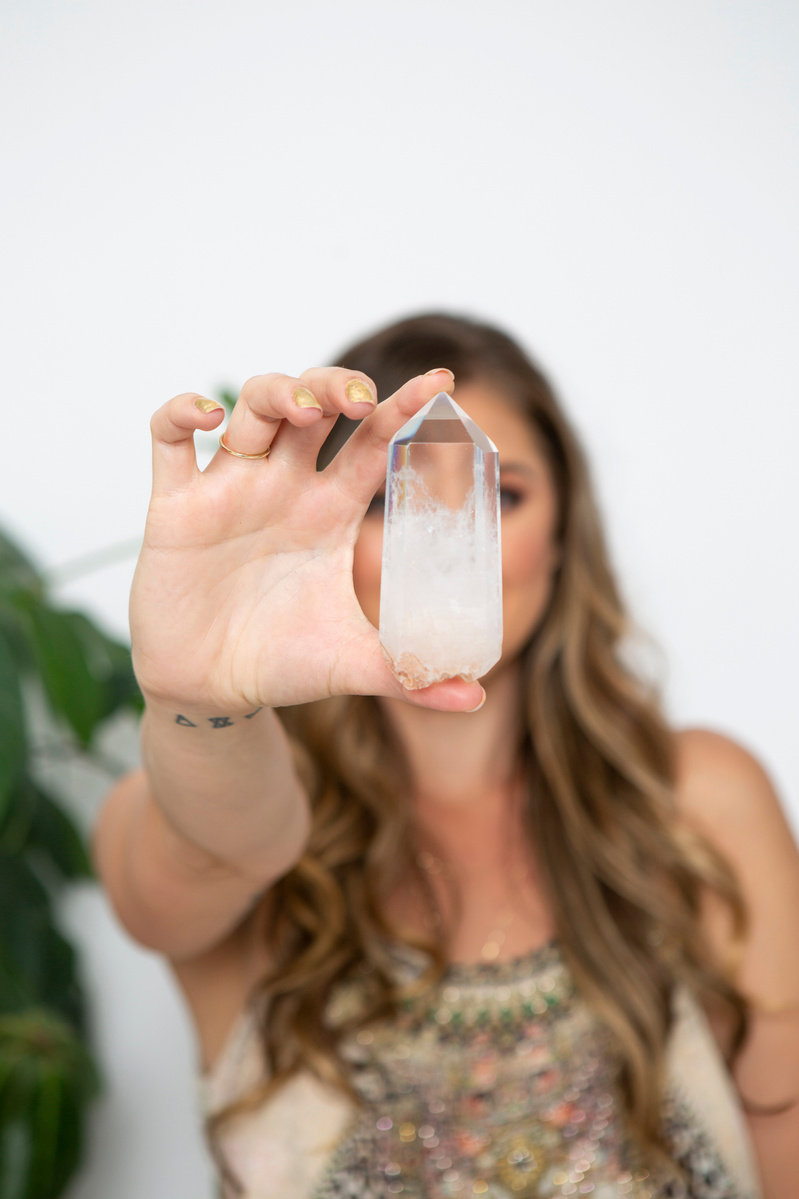 A young woman holds a crystal to the camera, obscuring her face