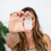 A young woman holds a crystal to the camera, obscuring her face