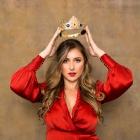 A strong young woman wears a red silk dress, she is about to place a gold crown on her head