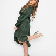 A glamourous young woman is wearing a long green dress, she kicks one heel up as she leans back and smiles