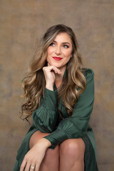 A young woman wears a green dress, she is sitting down and smiles off camera