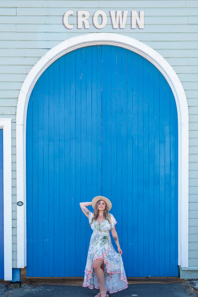 A young blonde woman stands in front of a bright blue door in a floral dress