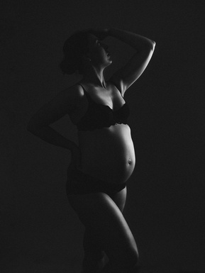 Slim, pregnant brunette poses powerfully with the light hitting her belly