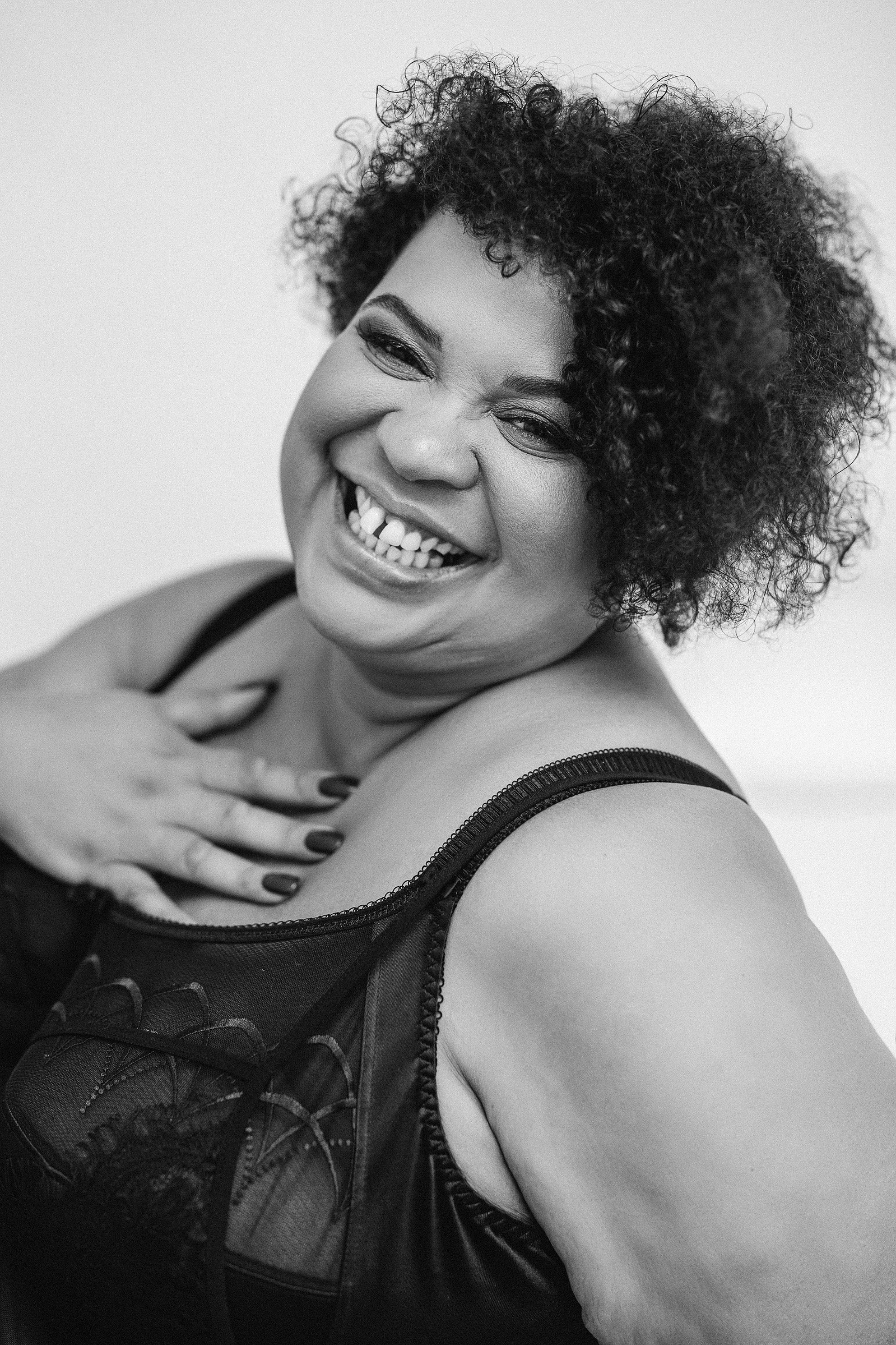 A beautiful woman of colour poses in her underwear, a hand is touched against her chest