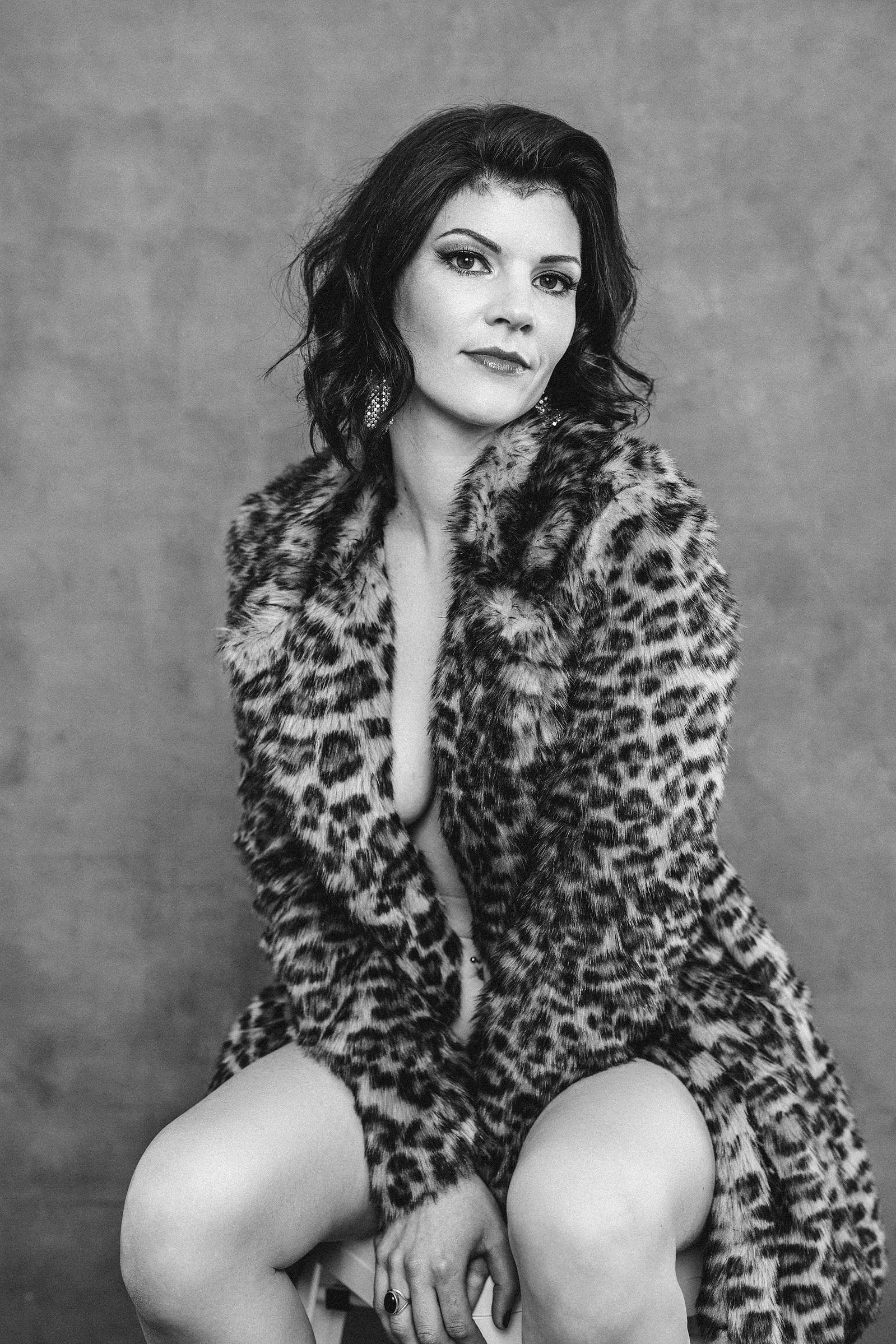 A glamourous brunette sits for a photo, she is wearing a leopard print fur coat