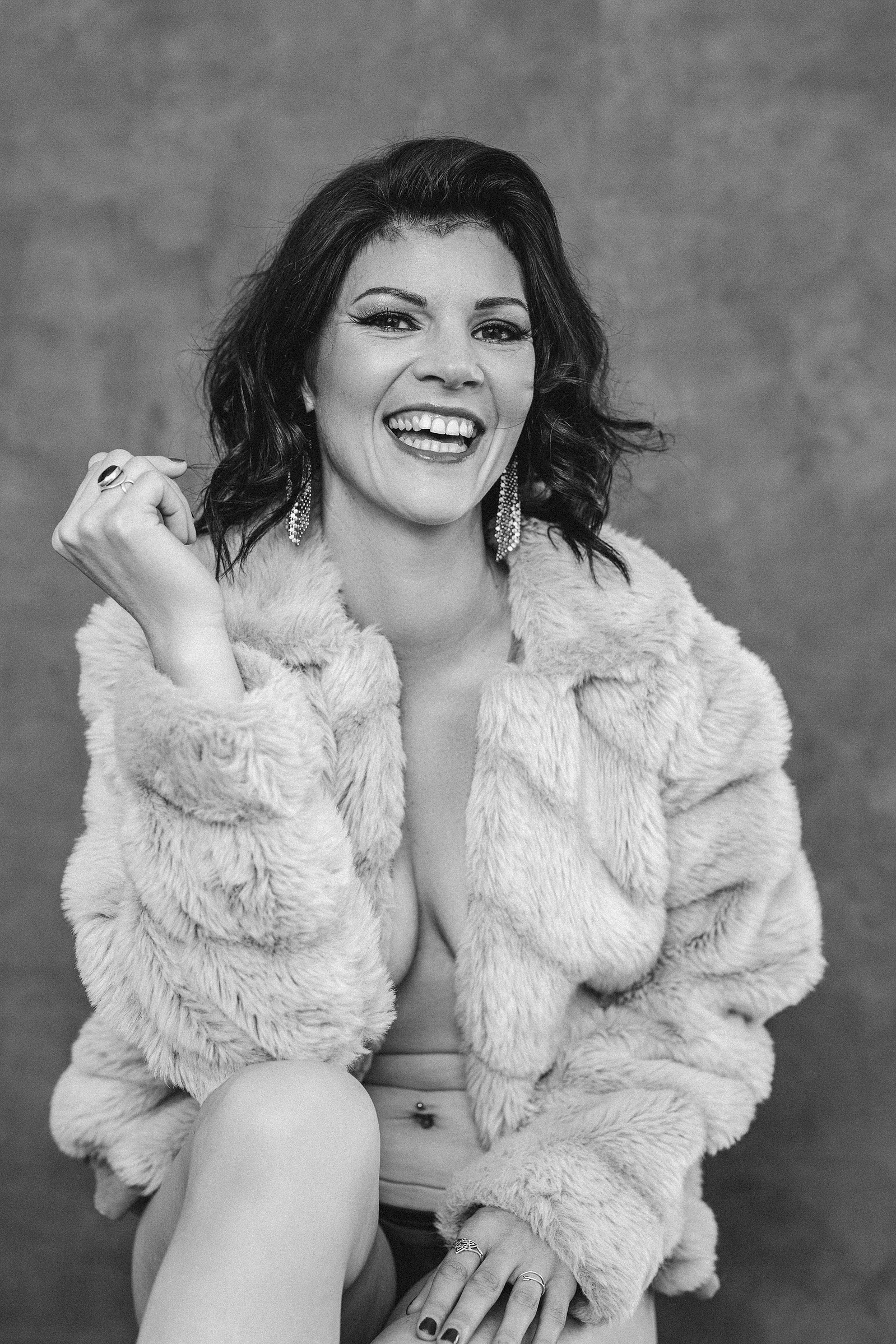 A brunette wears nothing but a fur coat, she is laughing