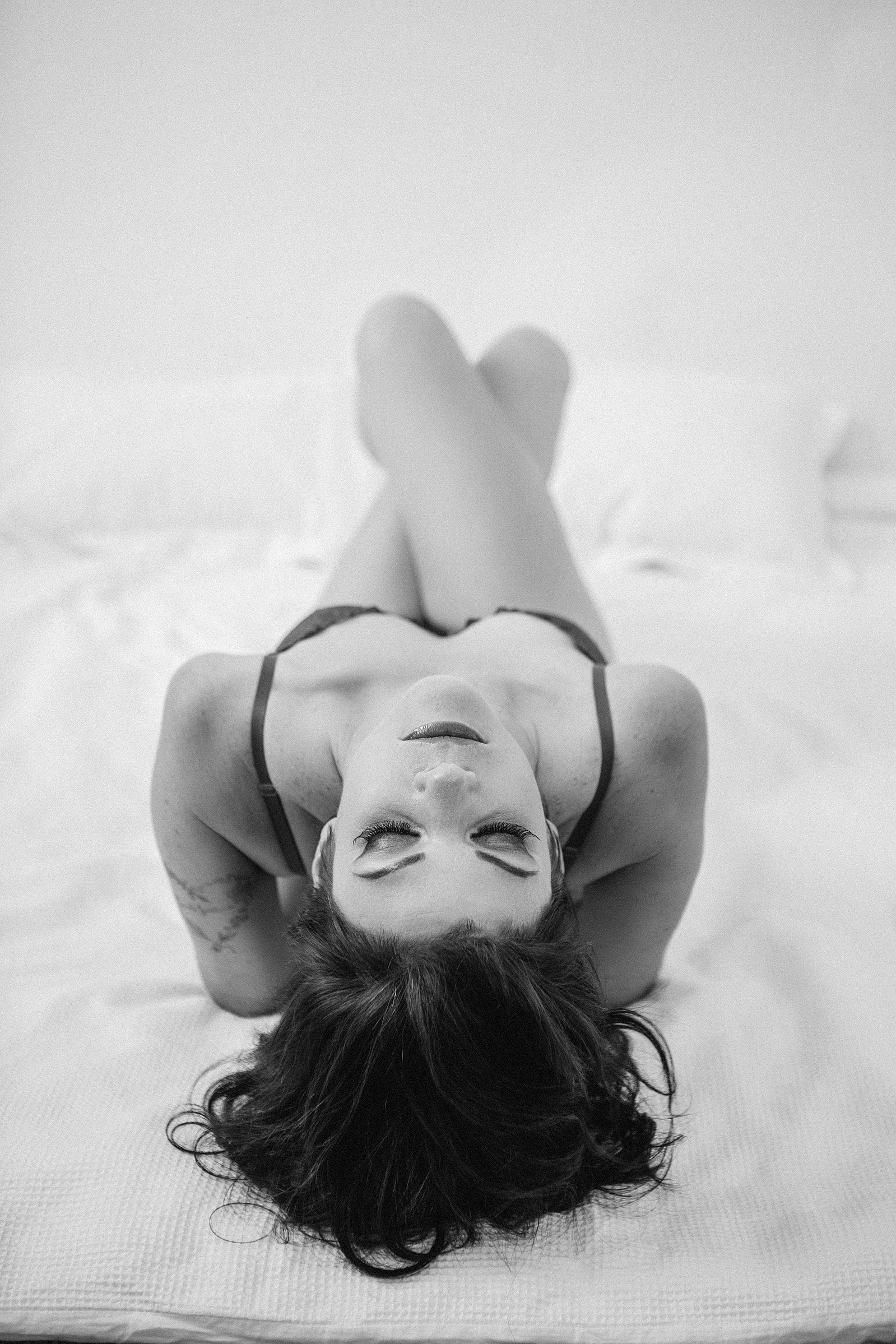 A woman poses boudoir style on a bed, she reclines and her head is thrown backwards