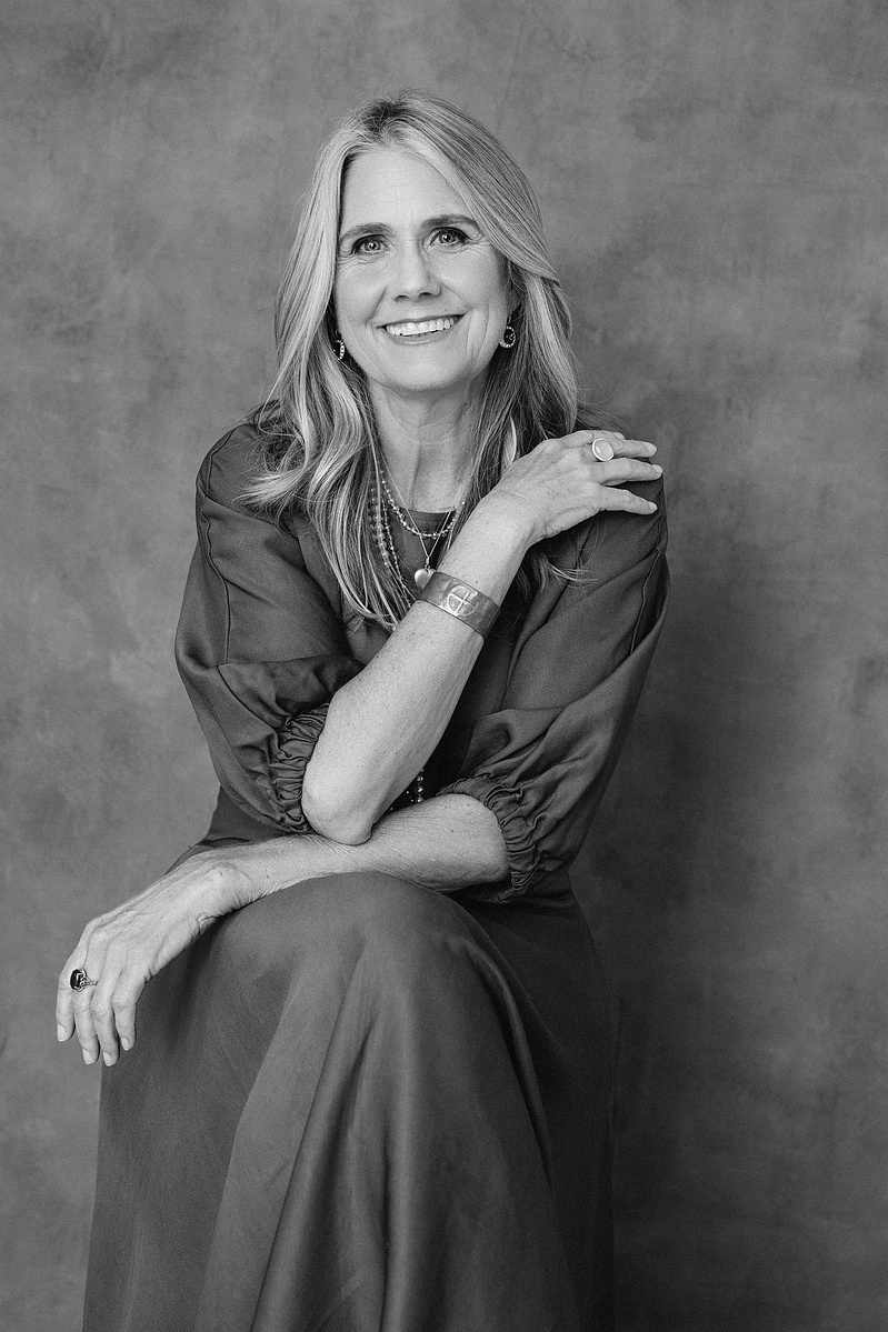 A slim woman with blonde hair sits for a portrait, her arms crossed over her torso