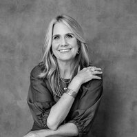 A slim woman with blonde hair sits for a portrait, her arms crossed over her torso
