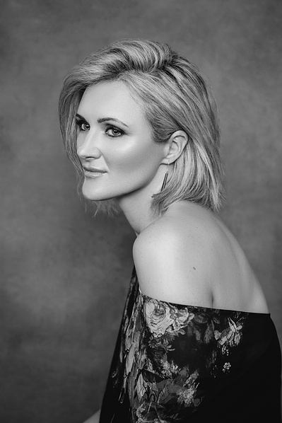 A stunning blonde woman with a bob wears an off the shoulder dress as she stares off camera