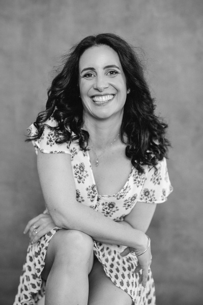 A woman with shoulder length brown hair, wearing a floral dress, smiling at the camera
